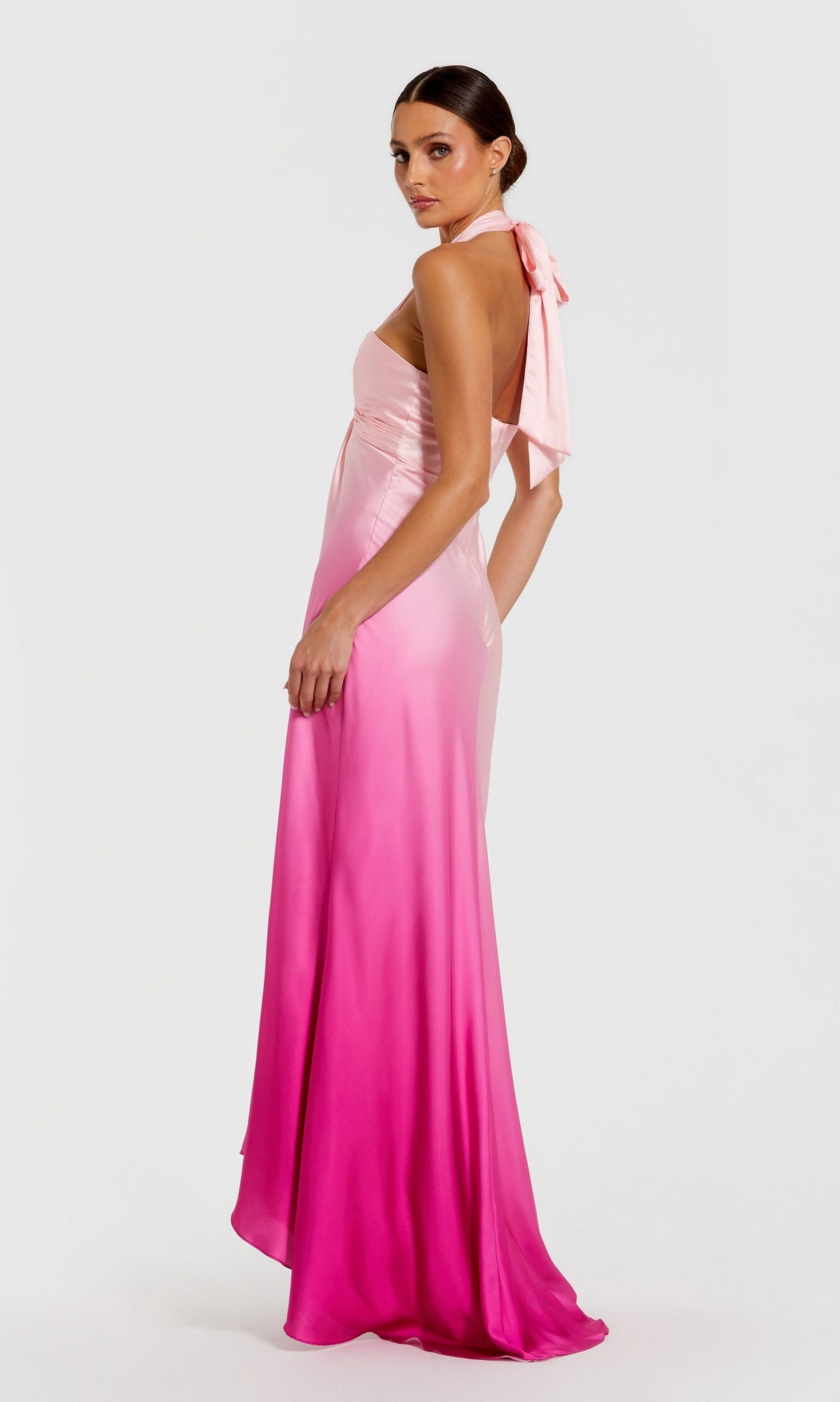 A woman models the Mac Duggal 68501, a pink floor-length charmeuse evening gown with a halter neck, exuding elegance and sophistication against a plain white background.
